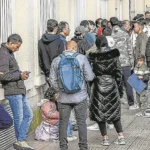 Inmigrantes hacen cola a las puertas de la administración.